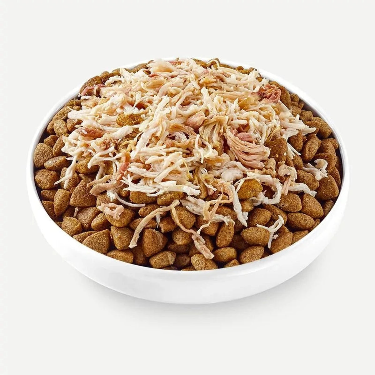 Cuenco con croquetas de pienso y topper de pollo desmenuzado añadido por encima, listo para servir
