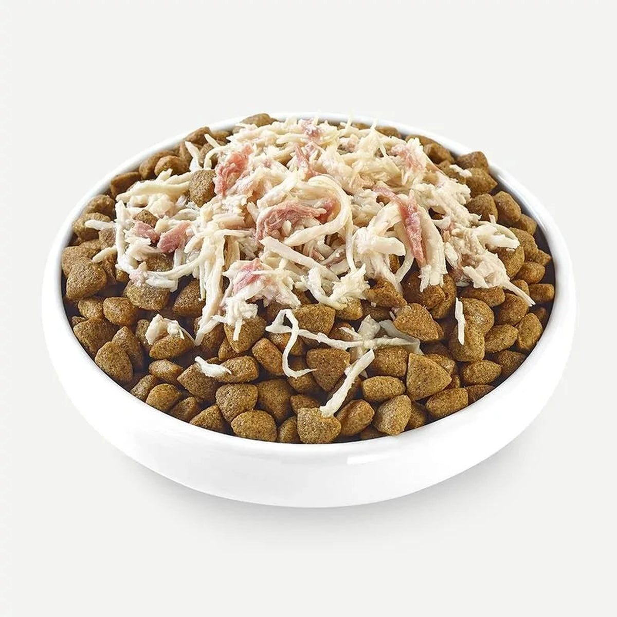 Cuenco con croquetas de pienso y topper de pollo desmenuzado añadido por encima, listo para servir