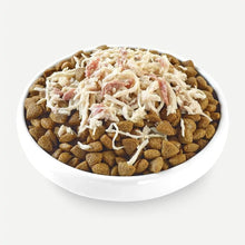 Cuenco con croquetas de pienso y topper de pollo desmenuzado añadido por encima, listo para servir