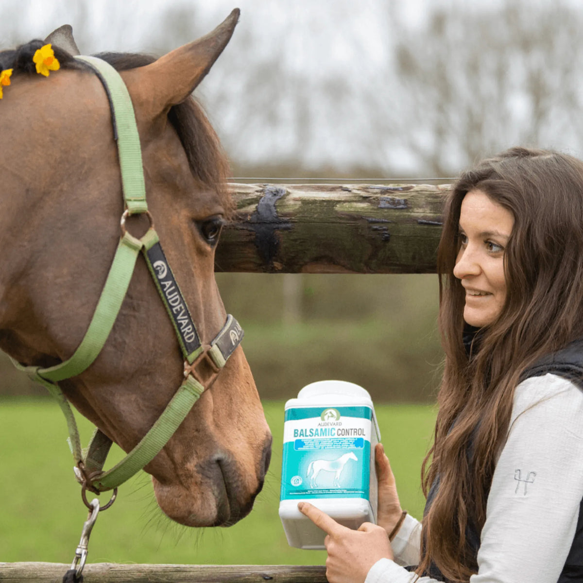 Mujer con el bote de Balsamic Control Audevard para caballos junto a un caballo con cabezada verde