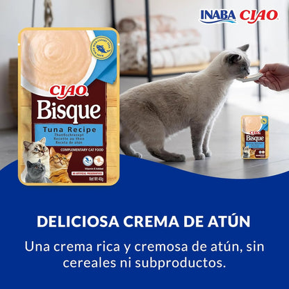 Gato gris tomando crema de atún de la mano de una persona, al lado de una bolsa de Ciao Bisque