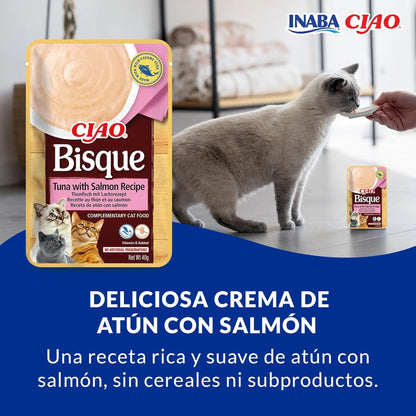 Gato gris tomando la crema de la mano de una persona, con la bolsa de atún con salmón al lado