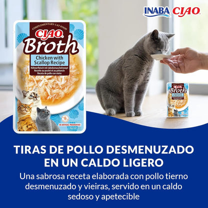 Gato gris tomando el caldo con tiras de pollo de la mano de una persona, junto a la bolsa de Ciao Broth