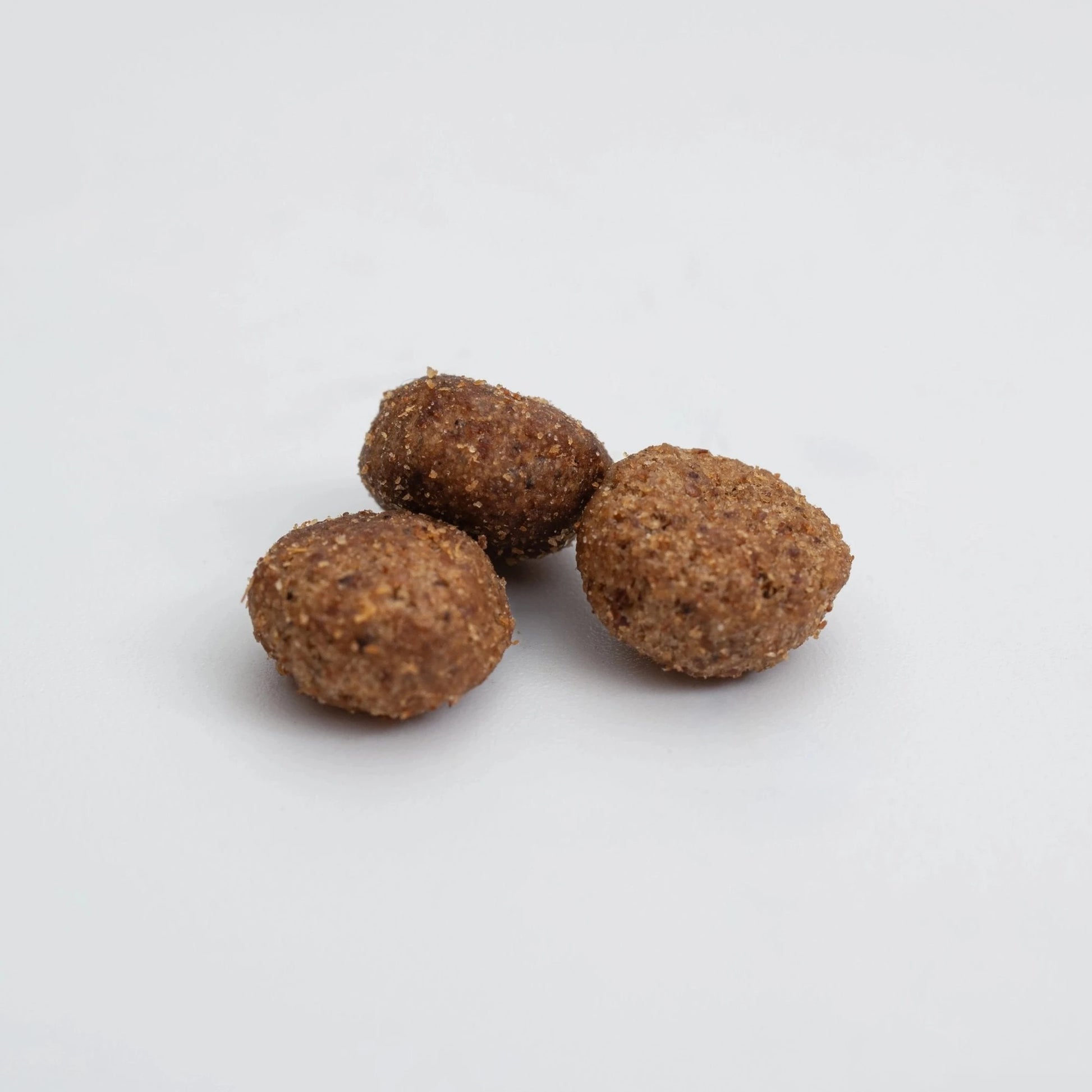 Primer plano de tres croquetas del pienso HPM Hypoallergy A2 para gatos, textura rugosa y forma oval